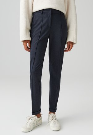 Schmale dunkelblaue Hose mit glatter Textur, mit Bügelfalten, Gürtelschlaufen und hochgekrempelten Säumen. Kombiniert mit weißen Sneakern.
