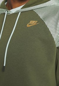 Oliwkowy hoodie z siateczką na kapturze, jasnoniebieskim sznurkiem i złotym logiem Nike. Miękka tekstura, casualowy design.