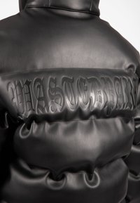 Μαύρο δερμάτινο τζάκετ νάιλον με ανάγλυφο λογότυπο "WASTED" στη πλάτη. Λείος επιφάνεια με γυαλιστερό φινίρισμα και φουσκωμένα τμήματα.