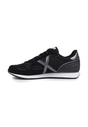 Zapatilla deportiva negra que presenta una mezcla de materiales de ante y malla, con acentos plateados, una superficie texturizada y una media suela blanca.