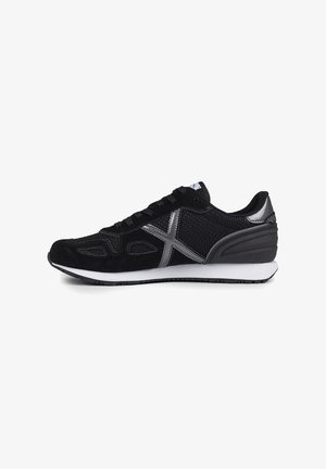 Zapatilla deportiva negra que presenta una mezcla de materiales de ante y malla, con acentos plateados, una superficie texturizada y una media suela blanca.