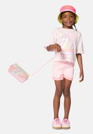 T-shirt graphique rose avec impression de licorne, associée à un short rose clair. Un sac bandoulière pailleté et coloré ainsi qu'un bob rose complètent le look.