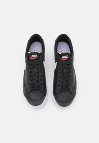 Svarta sneakers i läder med en texturerad grå mockadetalj, vit swoosh, röd logotyp och platta snören. Gummisula med en slät finish.