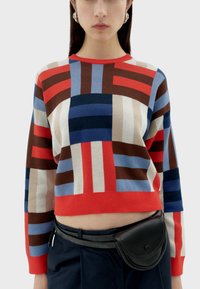 Un pull en tricot coloré présentant un motif géométrique en rouge, bleu et brun, avec un col rond et un design court.