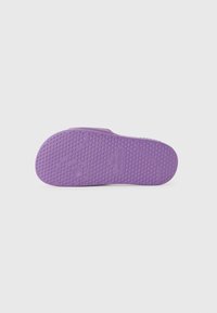 Violetinė guma su tekstūruotu sukibimu, apvalios formos ir įdubimais. Šalia kulno srities pažymėta "LACOSTE".