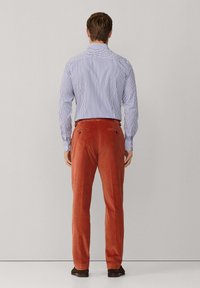 Men's striped blue and white button-up shirt paired with rust-colored corduroy trousers. Trousers feature two back pockets and textured fabric.