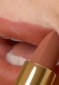 Lipstickrör med en guldbas, som visar en matt, neutral rosa nyans applicerad på läpparna. Slät textur och vinklad spets är synliga.