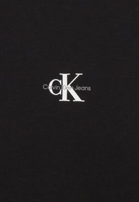 Svart bomull t-skjorte med hvitt "CK"-logo og teksten "Calvin Klein Jeans" under, sentrert, enkelt design. Glatt tekstur.
