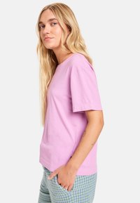 Ροζ βαμβακερό μπλουζάκι με κοντά μανίκια και στρογγυλή λαιμόκοψη. Διαθέτει βασικό σχέδιο και διακριτικό λογότυπο στο στήθος. Συνδυάζεται με καρό παντελόνι.