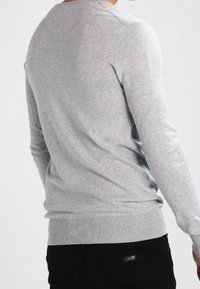 Szary długi sweter z długim rękawem wykonany z miękkiej bawełny, z okrągłym dekoltem i prążkowanym wykończeniem, o gładkiej fakturze i dopasowanym kroju.