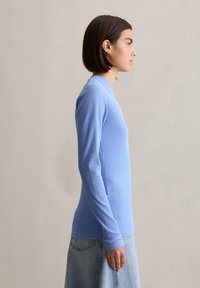 Top de manga larga acanalado en azul claro, con escote redondo y silueta ajustada. Textura suave, combinado con una falda de mezclilla.