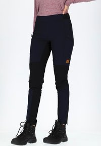 Schwarze und marineblaue Wanderhosen mit taillierter Passform, seitlichen Taschen und strukturiertem Stoff, kombiniert mit schwarzen Wanderschuhen.
