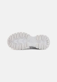 Semelle de sneaker blanche en matériau en caoutchouc texturé, présentant de profonds sillons et nervures pour une meilleure adhérence. Logo de marque notable visible au centre.