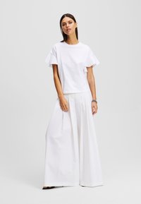 Tricou alb cu mâneci volănașe, asortat cu o fustă albă plisată, cu o textură netedă și design cu picioare largi.