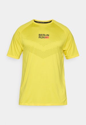 Camiseta deportiva amarilla de manga corta. Presenta "BERLIN RUN" y el logo de Nike en negro y rojo. Patrón texturizado en la parte superior delantera.