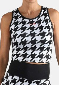 Mujer vestida con un top de corte corto sin mangas de estampado de pata de gallo en blanco y negro y leggings a juego con una ancha cinturilla negra.