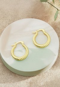 Guldtonade vridna hoopörhängen som visas på en slät rund yta, med en glänsande yta och ett säkert lås för bärande.