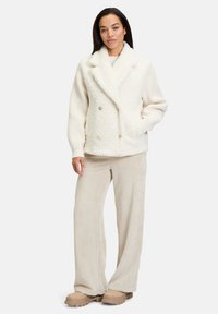 Hvid struktureret dobbeltbrystet jakke med sjalskrave, parret med beige corduroy bukser med bred ben og lyse støvler.