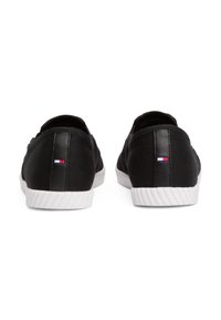Svarte lerrets sneakers med en glatt tekstur, hvite gummisåler og en liten trikolor-logo på baksiden av hælen. Rund form og lavprofil design.