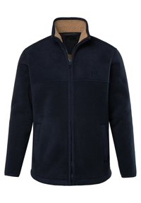 Chaqueta de forro polar azul marino con un cuello en contraste color beige, cierre con cremallera y dos bolsillos laterales. Presenta una textura suave y un detalle de logo en el pecho.