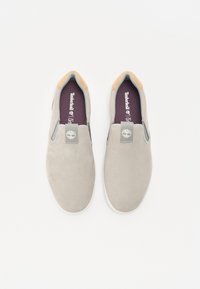 Grå semsket skinn slip-on sko med brunt lær på hælen, hvit gummisåle og et logo merket på vristen.