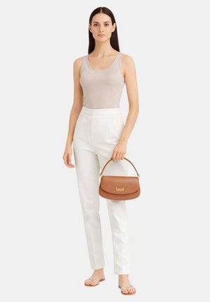 Donna con canottiera beige, pantaloni bianchi a vita alta e sandali che tiene una piccola borsa marrone con dettagli dorati.