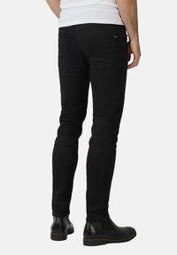 Czarne slim-fit dżinsy z denimu, charakteryzujące się gładką teksturą, tylnymi kieszeniami i niskim stanem. Połączone z czarnymi skórzanymi botkami za kostkę.