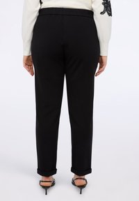 Černé kalhoty s elastickým pasem, rovný střih, ohrnuté manžety a hladkou, matnou texturou. Žádné viditelné vzory nebo kovové prvky.