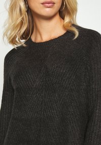 Pull noir en maille présentant un motif côtelé texturé, un col rond et une coupe décontractée, mettant en valeur une légère brillance du tissu.