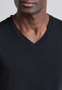 Schwarzes T-Shirt mit V-Ausschnitt aus glattem Baumwollstoff. Es verfügt über einen klassischen Schnitt mit lockerer Passform und einem tiefen Ausschnitt, der eine minimale Textur zeigt.