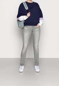 Námorně modrá oversized mikina s bílými a fialovými akcenty na rukávech, kombinovaná se světle šedými skinny džíny a bílými teniskami. Batoh součástí.