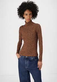 Braunes langärmeliges Rollkragenoberteil mit schwarzem Blumenmuster, taillierte Passform und weichem Material, kombiniert mit weiten blauen Jeans.