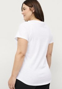 Witte t-shirt met korte mouwen, gemaakt van zacht katoen. Heeft een ronde halslijn en een iets langere achterkant voor een comfortabele pasvorm.
