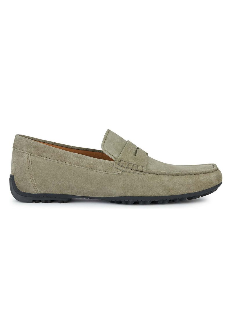 Mocasín de ante gris con detalles de costura, puntera redonda y suela de goma negra. Presenta una textura suave y un diseño clásico sin cordones.
