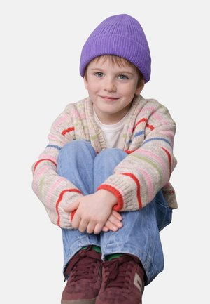 Colorful knit cardigan with red and green stripes, white t-shirt, blue jeans, purple beanie, and burgundy sneakers. Sitting position.