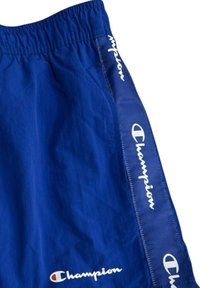 Pantaloni corti sportivi blu realizzati in tessuto leggero. Presentano un cinturino elastico e loghi bianchi "Champion" lungo la cucitura laterale.