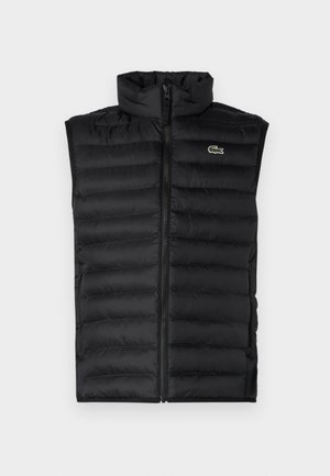 Juodas pūkinis liemenė su aukštu apykakle, užtrauktuku ir horizontaliomis juostomis. Ant krūtinės yra mažas Lacoste krokodilo logotipas.