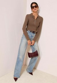Braun gerippter langärmeliger Poloshirt mit Knopfdetails, hellblaue weite Jeans, dunkelrote lackierte Handtasche und spitze High Heels.