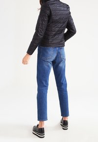 Sort, quilted let blazer med stående krave, parret med blå straight-leg jeans og sorte sko med hvide striber på sålerne.