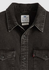 Cămașă din denim negru cu un design western relaxat, având un guler ascuțit, închidere cu butoane în față și un singur buzunar pe piept cu închidere cu button.