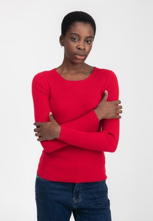 Rotes, geripptes Langarmoberteil mit runder Ausschnittform, kombiniert mit dunkelblauen Jeans. Die Stoffoberfläche ist glatt, enganliegend und leicht dehnbar.