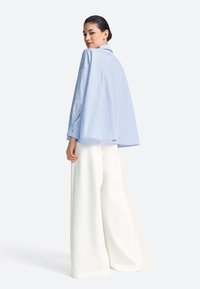 Modrá a biela pruhovaná nadmerná košeľa s voľným strihom, gombíkmi na manžetách a špicatým golierom, kombinovaná so širokými bielymi nohavicami.