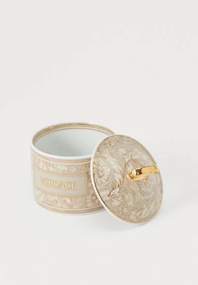 Balta porcelāna burka ar zelta dekorācijām, rotāta ar smalkiem ziedu rakstiem. Vāciņam ir zelta rokturis; centrā atrodas "VERSACE" nosaukums.