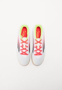 Scarpe da ginnastica bianche con una trama a righe, strisce nere, lacci rosa vivaci e dettagli verde neon sul tallone. Suola in gomma.