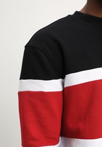 Felpa a righe nera, rossa e bianca con scollo rotondo. Presenta ampie righe orizzontali e un tessuto morbido e texturizzato.