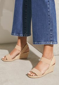 Bežové wedge sandály s elastickými pásky a tkanými juty detaily. Design s otevřenou špičkou; texturovaný povrch; kombinované s širokými džíny.