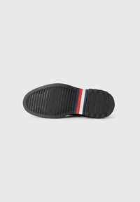 Zwarte rubberen schoenzool met horizontale ribbels, voorzien van een streep patroon in rood, wit en blauw nabij de hiel, met een vlak ontwerp.
