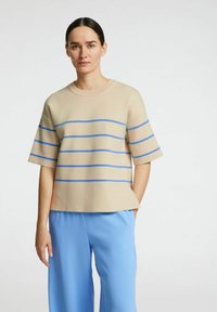 Top beige a maniche corte con strisce orizzontali blu, scollatura tonda, vestibilità ampia. Abbinato a pantaloni larghi azzurri.