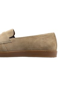 Scarpa slip-on in suede beige con punta arrotondata, caratterizzata da una patta pieghevole e suola in gomma. Texture liscia e dettagli di cucitura minimali.