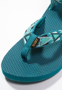 Sandal in blu teal Teva con cinturini in tessuto a fantasia e suola testurizzata, progettato per un uso casual all'aperto.